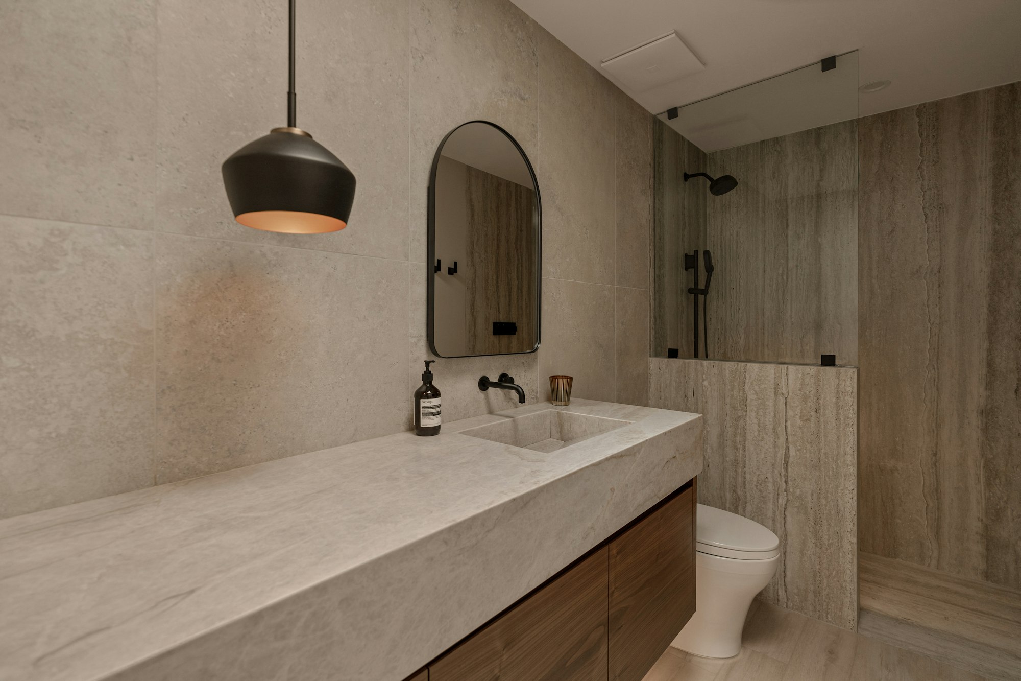 Baño de piedra beige en gran formato con lámpara negra