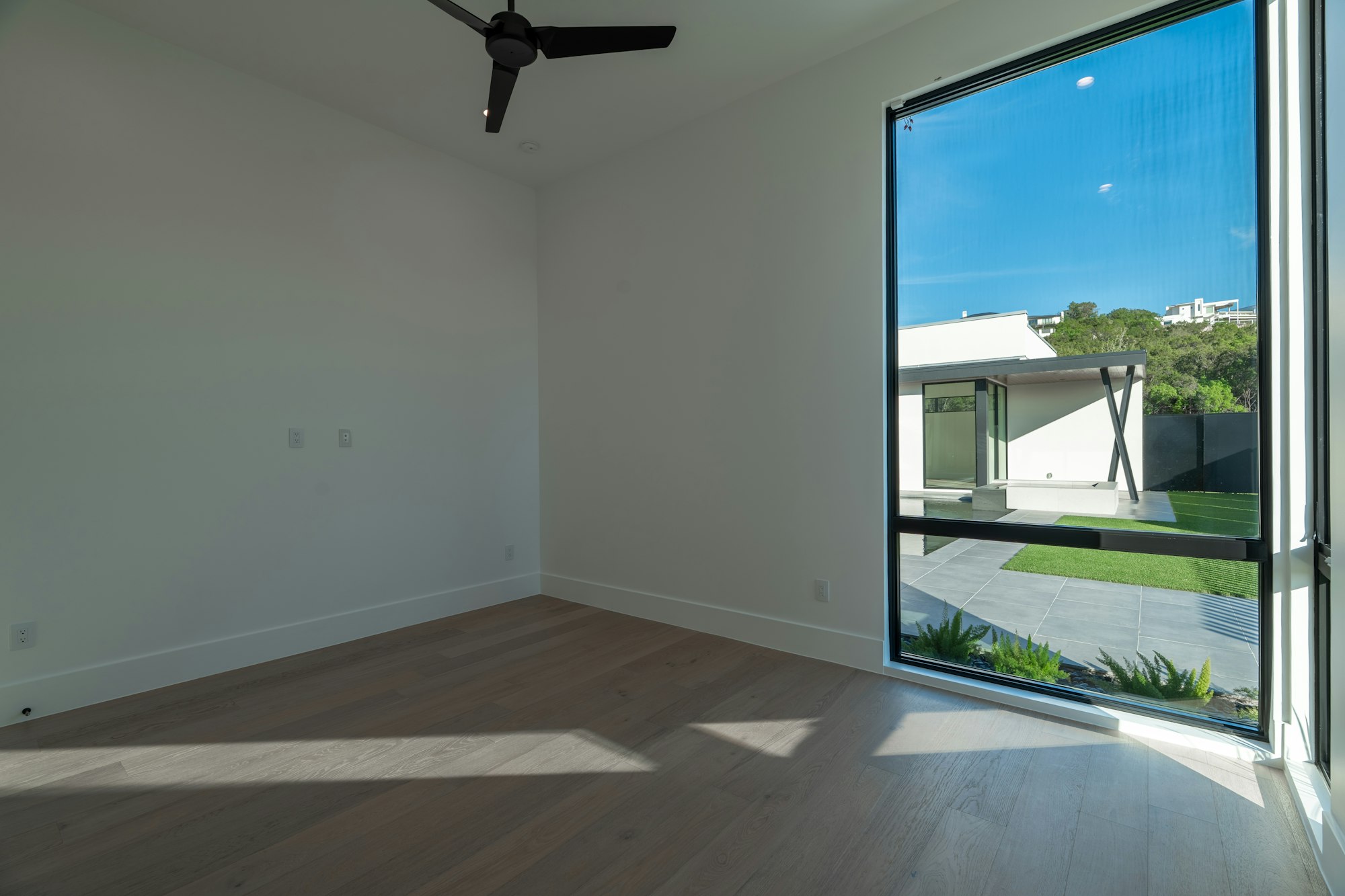 Estancia vacía con pavimento de madera y un gran ventanal al jardín