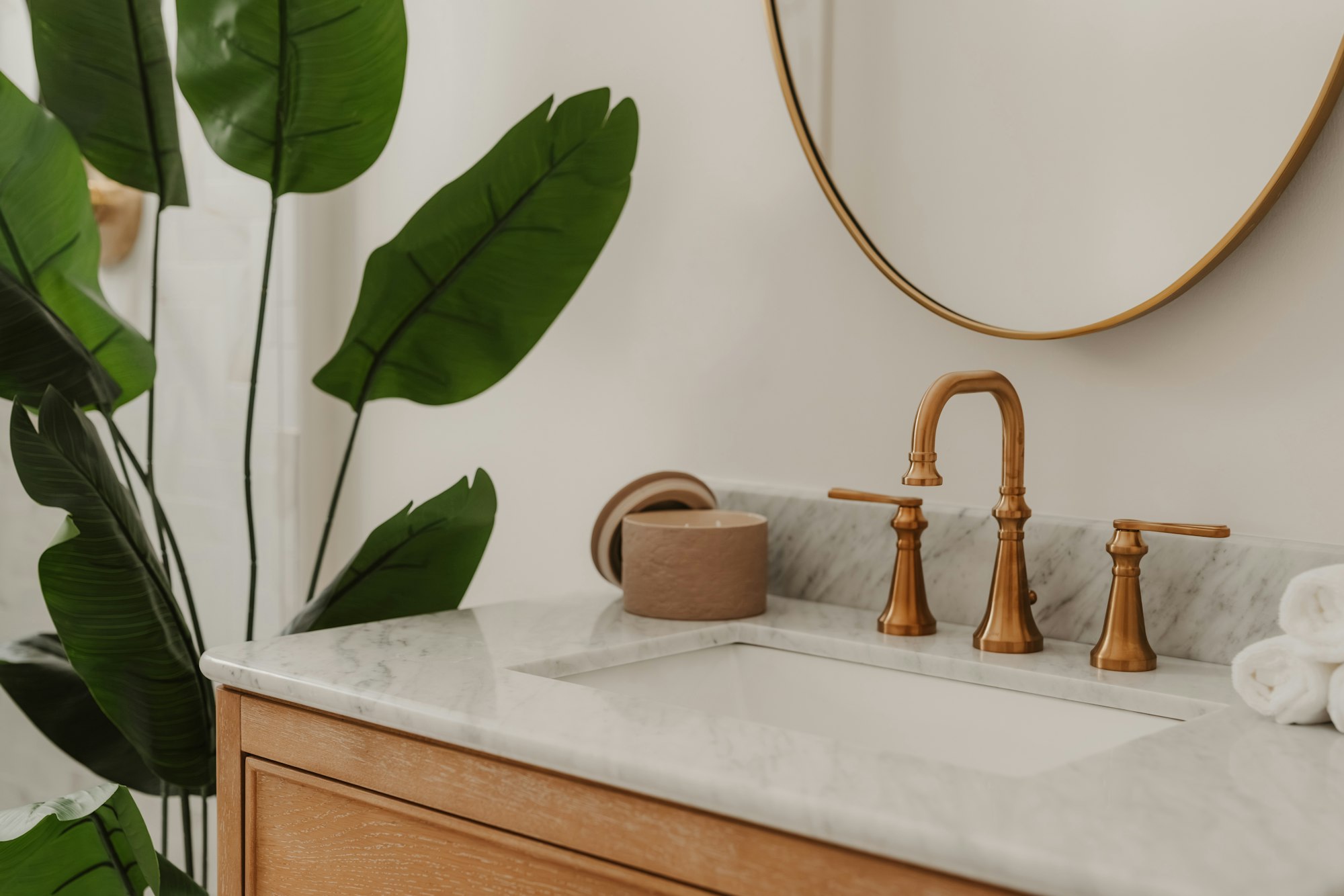 Lavabo de mármol con grifería dorada, espejo redondo y planta
